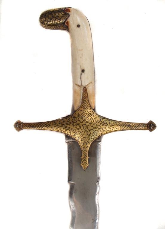 A FINE MUGHAL SHAMSHIR SABER: An exceptional example, the faceted steel pommel cap and guard thickly inlaid overall with gold in flowering vine motifs. The broad, curved blade forged of fine, actively-patterned wootz, with flamboy