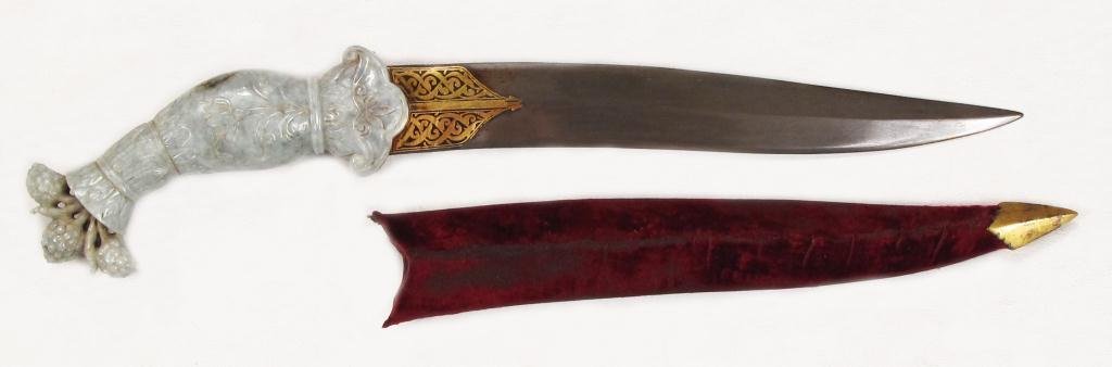 A MUGHAL JADE-HILTED KHANJAR DAGGER: The grip carved of a single section of pale green jade with dark mottling, with swollen grip and flared pommel surmounted by with three fully-modeled clumps of grapes on vines, the surface carved with