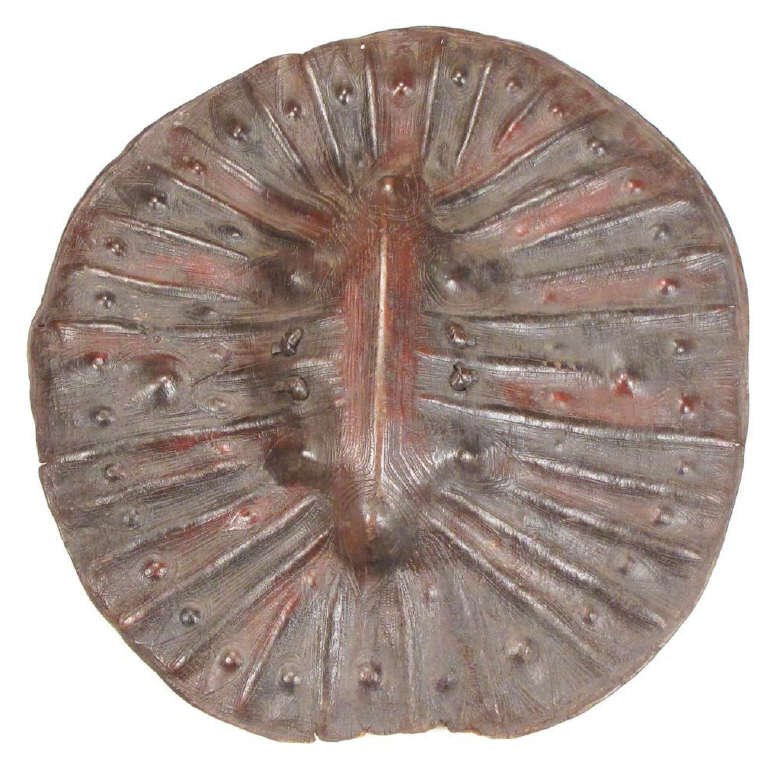 AN ETHIOPIAN ARUSSI SHIELD: Of characteristic form, molded in thick hide with a complex series of ridges bordered in knobs, pigmented in brownish red and black, and elaborately tooled overall in geometrical motifs. The reverse w