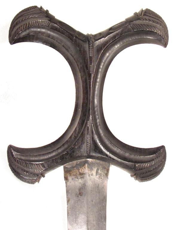 A BEJA DAGGER: A quality example, the distinctive ebony grip with complex geometrical carving, the robust double-edged blade with central ridge. In its tooled hide scabbard with filigreed silver mounts. Latter 19th