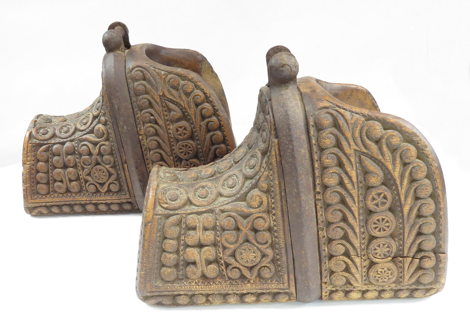 A RARE PAIR OF CHILEAN HUASO STIRRUPS: Each carved of a single section of wood and incised in complex geometrical motifs with finely inlaid iron mounts and pierced brass finials. 19th century. Minor wear, small cracks, steel patinated. Ove