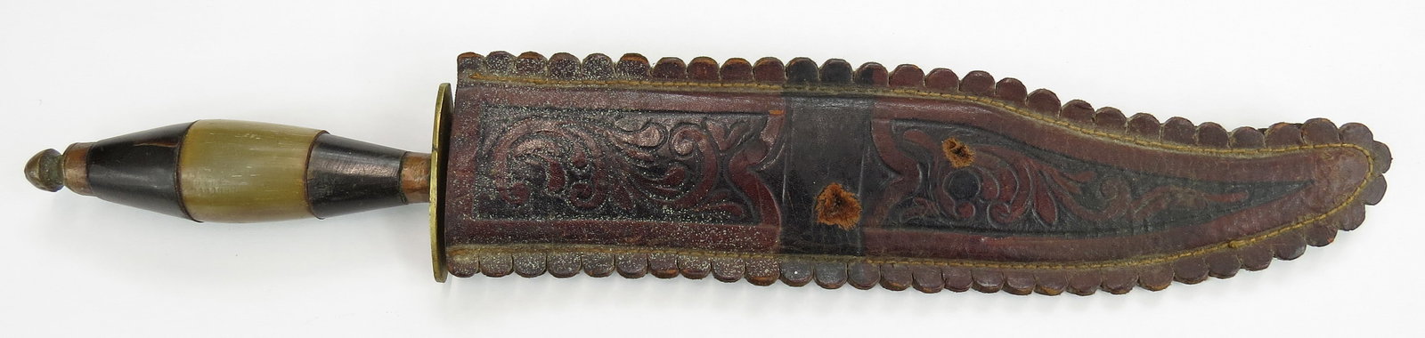 A MEXICAN BOWIE KNIFE: Revolutionary period, with segmented horn grip and brass guard, pommel and ferrule, the broad blade with clipped tip, signed with a stylized D. In its tooled leather sheath with scalloped borders. Ear