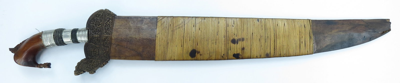 A MORO BARONG SWORD: The crested grip well-carved of banati wood, the ferrule with panels of woven coir. The massive, handforged blade showing clear patternwelded construction. In its wooden scabbard with finely-carved pa