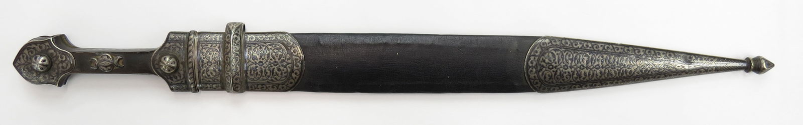 A CAUCASIAN KINDJAL DAGGER: The horn grips with well-engraved and nielloed silver mounts. The handwrought, straight, double-edged blade with double fullers with etched decoration and long tip. The leather-covered wooden scabbard