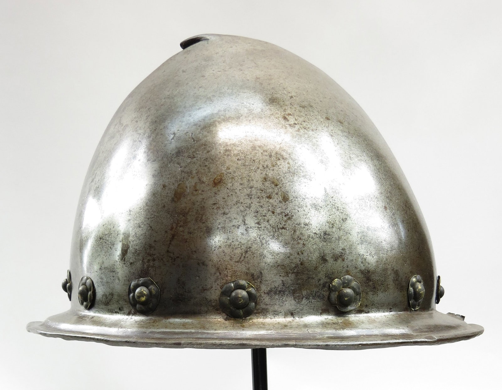 A NORTHERN ITALIAN CABASSET HELMET: An above average example, forged in one piece with pronounced ridge to the skull terminating in a pearstalk, with most original finish and brass rosettes intact with much original leather band intact.