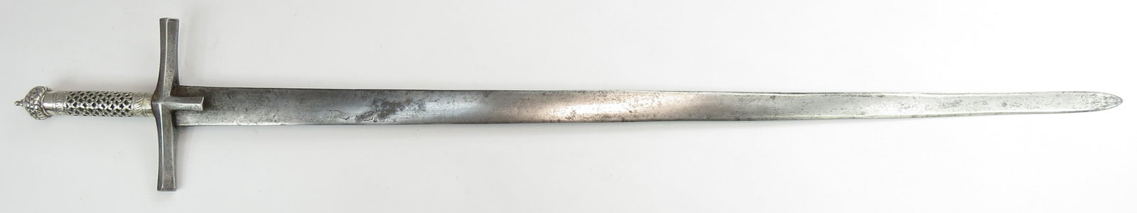 A RARE SUDANESE KASKARA BROADSWORD: The pommel and grip wrought in one piece of silver, with characteristic domed pommel, pierced and engraved throughout with latticework to one side and an open panel to the other with green silk velvet