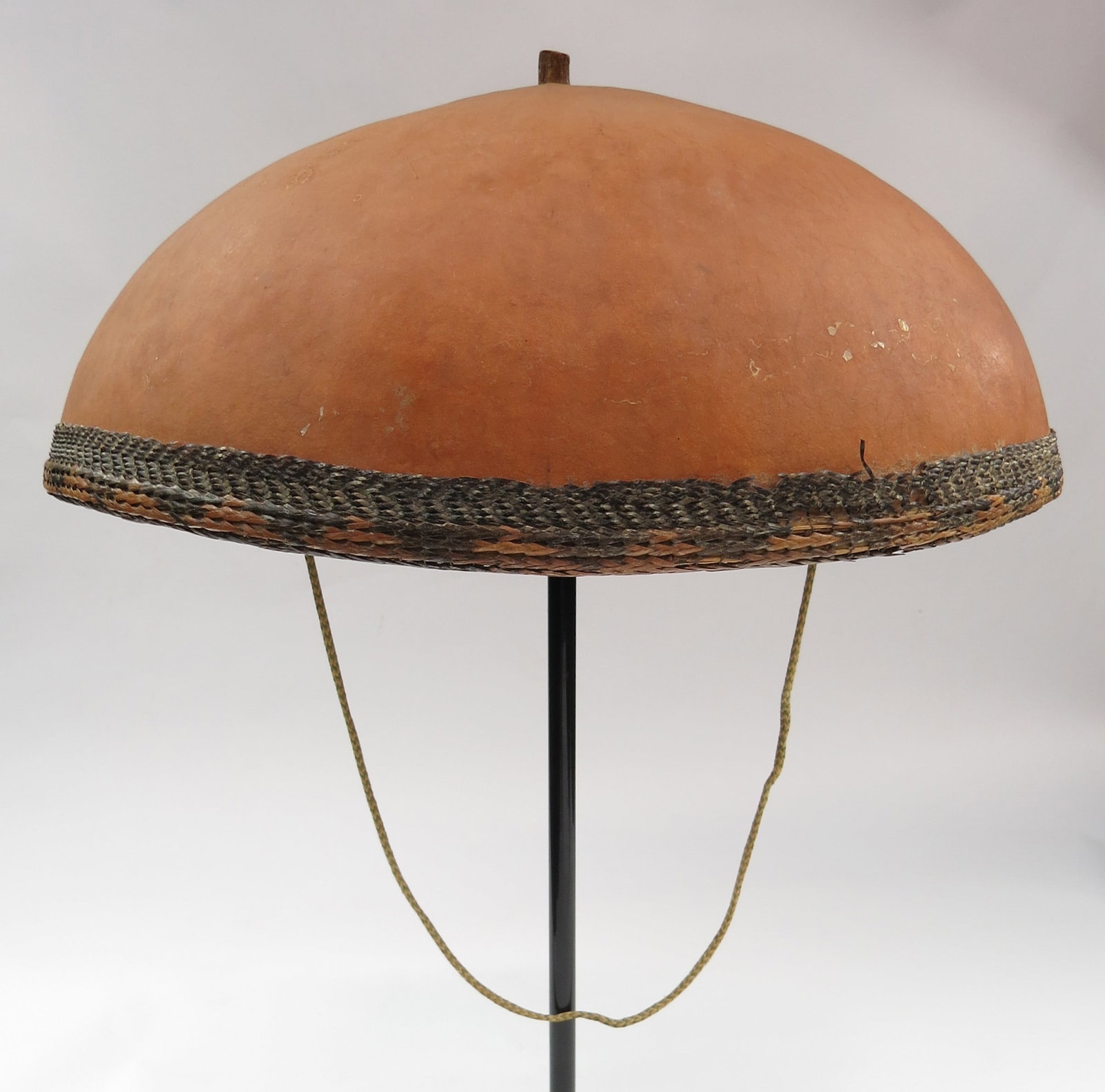 A RARE PHILIPPINES KATTUKONG CAP: Ilocano work, of characteristic form, carved of a single section of large gourd with intricately woven binding and liner of rattan. Retains its chinstrap. Late 19th-20th century. Overall height 15cm/ 