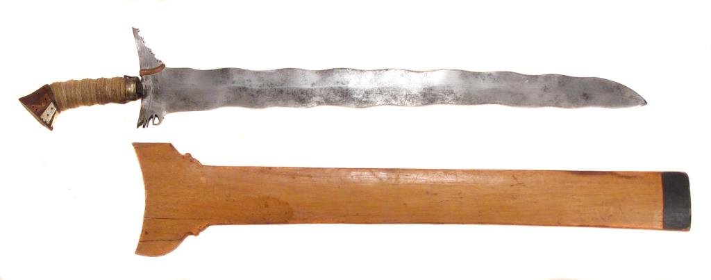A MORO KRIS SWORD: Wooden cord-wrapped grip, the pommel inlaid with mother of pearl panels engraved with okir motifs. The waved blade with copper baca-baca. In its wooden scabbard decorated en suite with the grip. Early