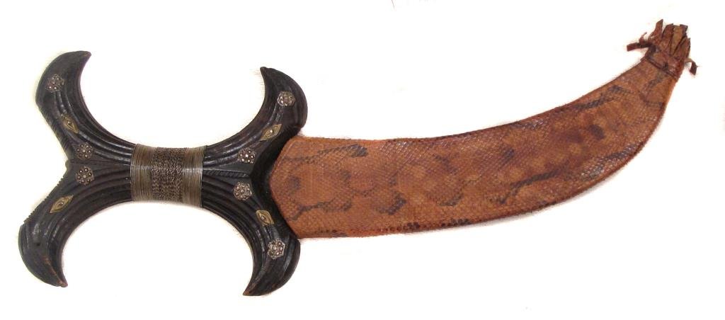 A HADENDOA DAGGER: With typical hardwood grip, carved and studded with silver. The curved, double-edged blade handforged.In its snakeskin scabbard.Late 19th century. Light wear. Overall length 31.2 cm. Condition II