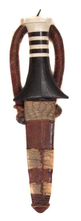 A SUDANESE ARM DAGGER: With ebony and elephant handle and broad blade, the leather scabbard with braided armband. Late 19th century.Losses to pommel.Overall length 23 cm. Condition IV