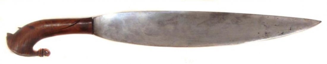A MORO BARONG SHORTSWORD: With carved exotic hardwood grip and broad, handforged, layered blade. Latter 19th century. Losses to grip.Overall length 61 cm. Condition IV