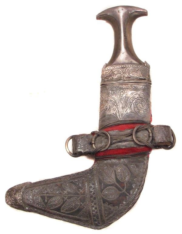 AN OMANI KHANJAR DAGGER: With elaborately engraved silver mounts and horn grip, the curved blade with distinct central ridge. In its matching scabbard.Late 19th-early 20th century. Ferrule cracked. Overall length 29.5 cm. Con