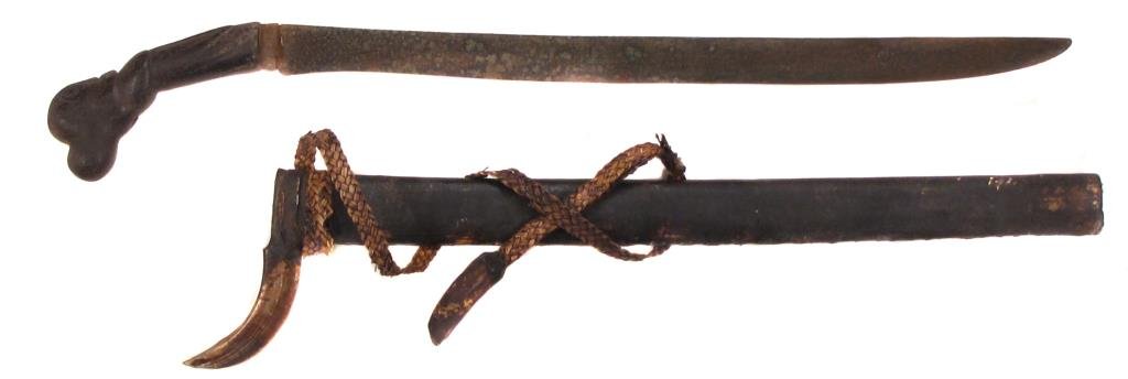 AN INDONESIAN SWORD: With carved wood handle and handforged blade. Wooden scabbard with tusks.Early 20th century. Worn, blade pitted. Overall length 61 cm. Condition IV