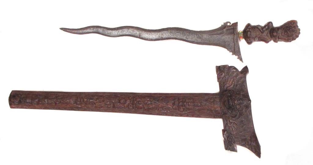 A BALINESE KRIS: A large example with finely carve grip and waved, actively-patterned Damascus blade. In its matching scabbard.Mid-20th century.Overall length 60.3 cm. Condition I
