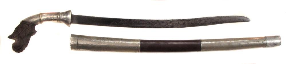 AN INDONESIAN PARANG SWORD: Fancy carved horn handle with handforged watered blade and silver mounts. In its matching scabbard.Mid 19th century. Wear and repairs to silver. Overall length 69.6 cm. Condition III