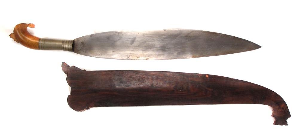 A MORO BARONG SHORTSWORD: With carved and crested exotic hardwood grip and broad, handforged blade, the wooden scabbard with well-carved okir motifs. Late 19th - early 20th century.Overall length 62 cm. Condition II