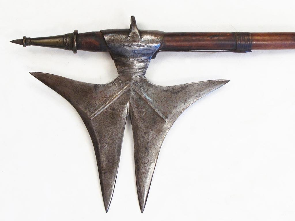 A RARE INDIAN BATTLEAXE: A form endemic to the Bhil people of Central India, the steel head forged with multiple points, the socket engraved and wrought with a pronounced flange. On its hardwood haft with iron and brass mount