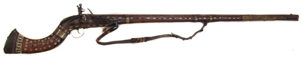 AN AFGHAN JEZAIL MUSKET: With characteristic curved hardwood stock, profusely inlaid with bone and ebony in geometrical motifs.With large flintlock mechanism, the barrel retained by brass bands.Retains its leather sling.Latte
