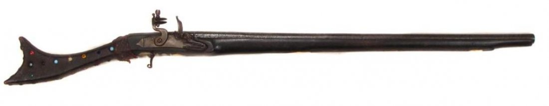 A GREEK KARIOPHILI FLINTLOCK MUSKET: Rarely encountered in carbine length, the butt covered in tooled leather and set with glass gems, the lock of local manufacture, the barrel with octagonal breech inlaid in silver vegetal motifs overal