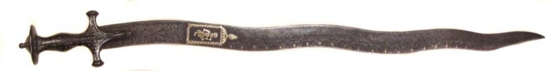 AN INDIAN TULWAR SWORD: The iron hilt with substantial remains of silver inlay, the waved blade chiseled and inlaid with a large cartouche containing the Hindu god Krishna. 19th century. Worn.Overall length 80 cm. Condition 
