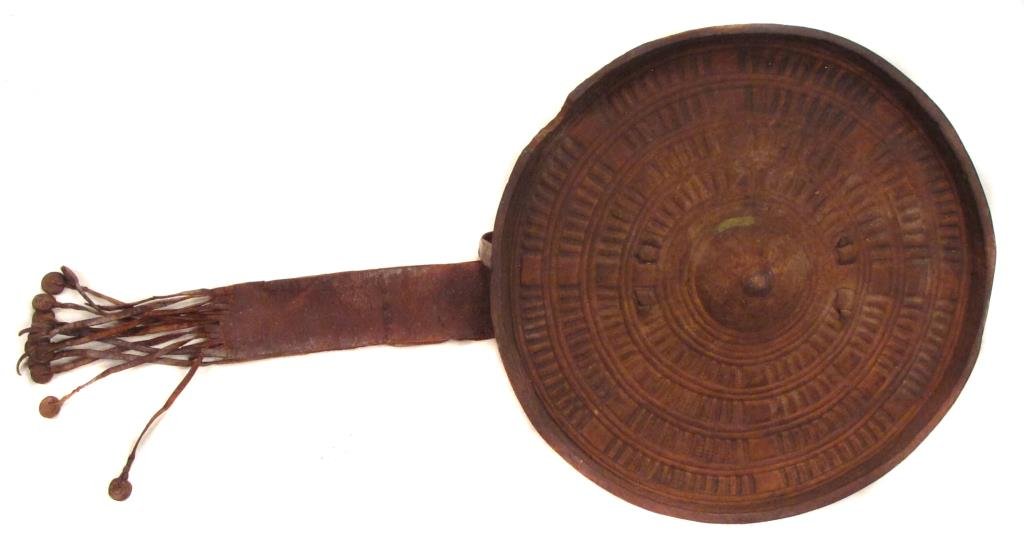 AN ABYSSINIAN HIDE SHIELD: Of molded rawhide with separately-applied grip, the obverse with characteristic geometrical tooled motifs overall.Retains its pendent strap.Mid 19th century.Diameter 31 cm. Condition II