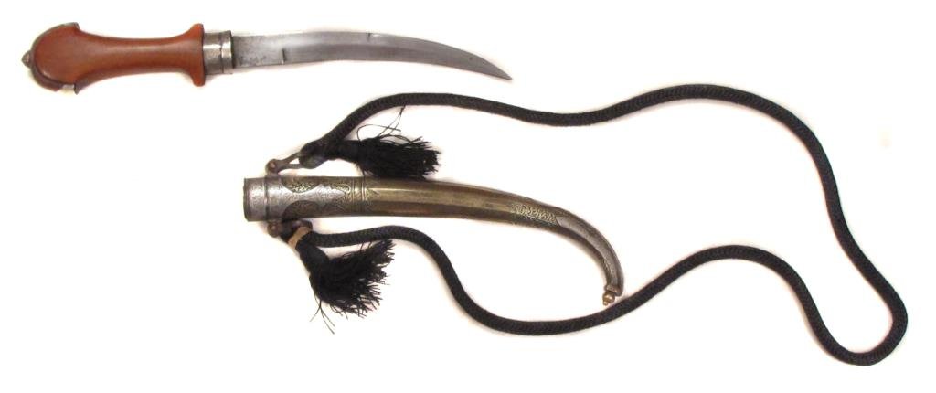 A MOROCCAN KOUMIYYAH DAGGER: Of characteristic form with flared wooden grip, the arched pommel and scabbard wrought entirely of brass with finely-engraved silver appliques. The curved blade with central ridge.Retains its woven su