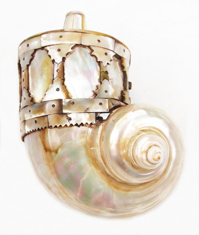 AN INDIAN BARUTDAN POWDERHORN: The body formed of a large, polished sea snail shell, the upper section and spout formed of additional profiled shell plaques. The suspension ring of copper.Early 17th century. Light wear. Overall len