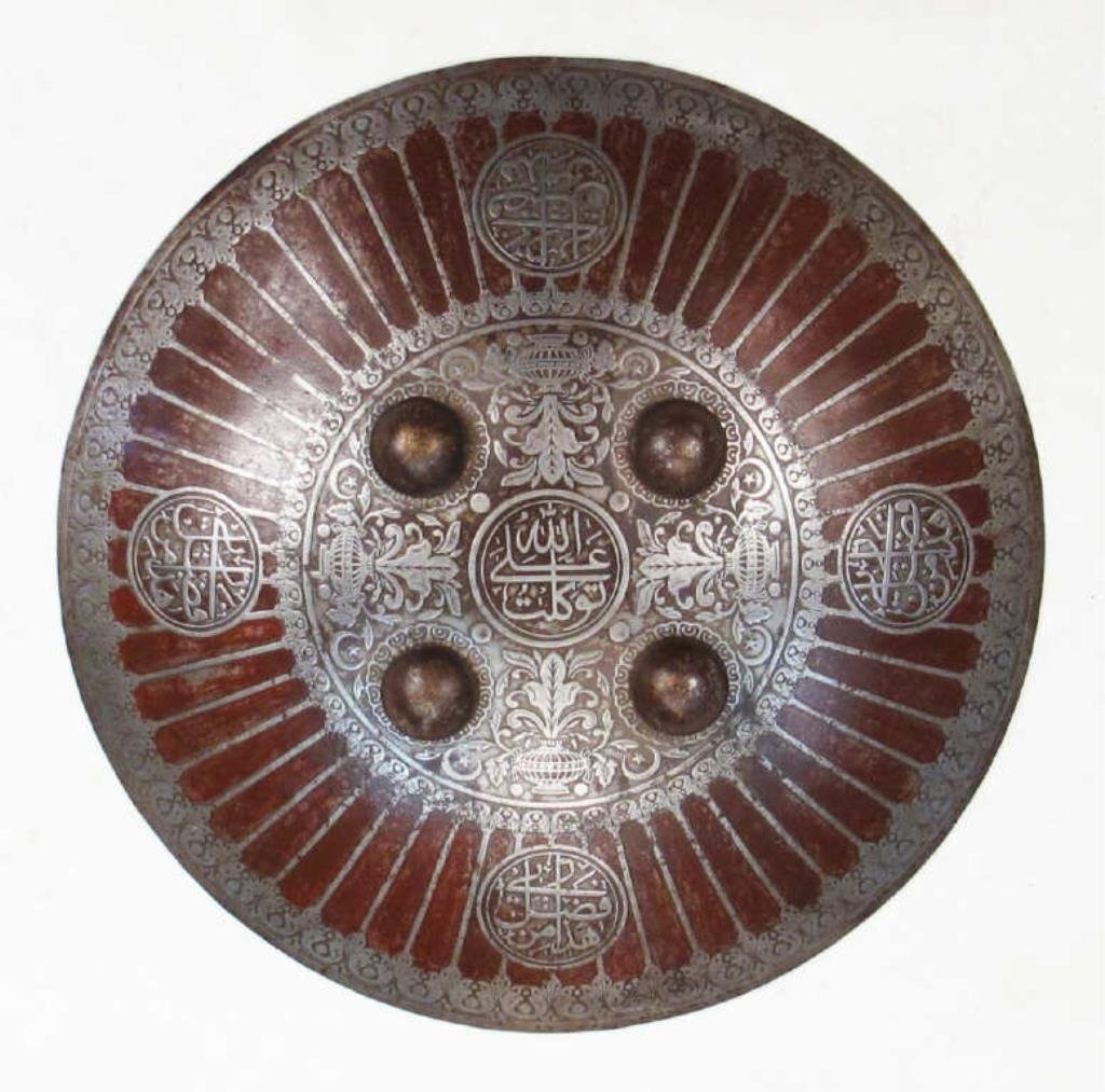 AN OTTOMAN KALKAN SHIELD: A rare example, wrought in steel and superbly chiseled at the center in flowering vines issuing from vases, together with five circular cartouches, the central one inscribed ALLAH, ALI, TUKLAT! The pe