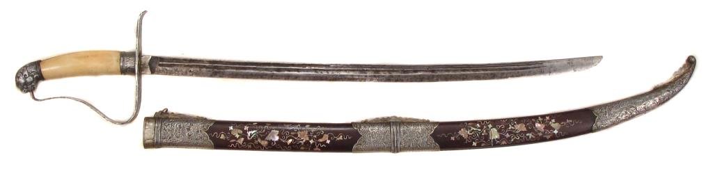 A VIETNAMESE GUOM SABER: A very rare type of characteristic form, the silver-mounted hilt with embossed and engraved monsterhead pommel and ferrule, with elephant grip, the silver guard with broad knucklebow.Single-edged, bif