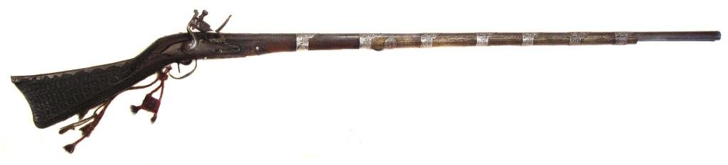 A RARE OTTOMAN MUSKET: A rarely-encountered form from Rumelia (modern Bulgaria) with hardwood stock, the flattened butt of elongated triangular section, profusely carved overall with a profiled steel reinforce along the com