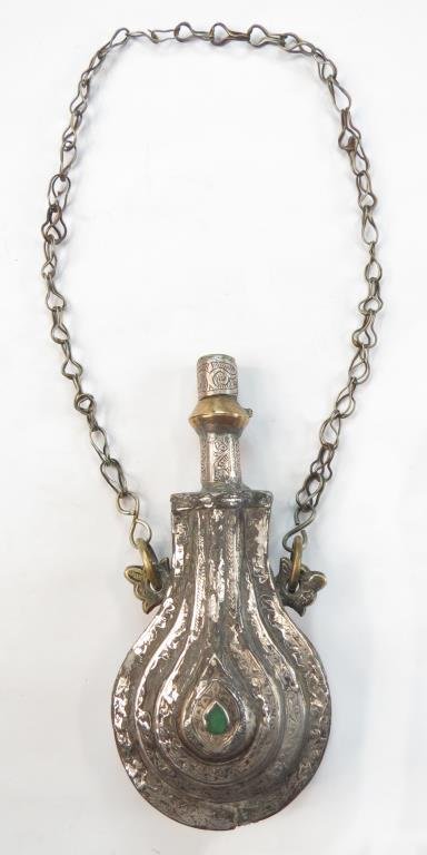 A MOROCCAN POWDER FLASK: Wrought of brass and overlaid with silver, well-engraved overall with suspension chain intact. Set with a green stone. Mid- 19th century. Worn. Overall length including chain 49 cm._x000D_ Condition I