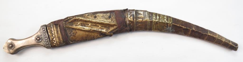 AN ARAB KHANJAR DAGGER: Hijazi type, mounted in engraved brass, the pommel of characteristic form with raised bosses. The blade broad, lightly curved and double-edged, In its brass-covered wooden scabbard. Mid-19th century.