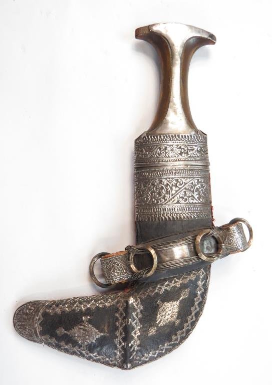 AN OMANI KHANJAR DAGGER: Of typical form, the horn grip with flared pommel and embossed silver ferrule. The curved, double-edged blade with central rib, wooden scabbard with heavy silver-embroidered leather covering and large