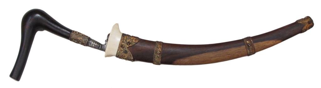 A SUMATRAN RENCONG DAGGER: With dark hardwood grip of characteristic form and gilt filigreed ferrule, the recurved pamor blade with profiled forte. In its matching scabbard with elephant locket and gilt filigreed mounts wet wit
