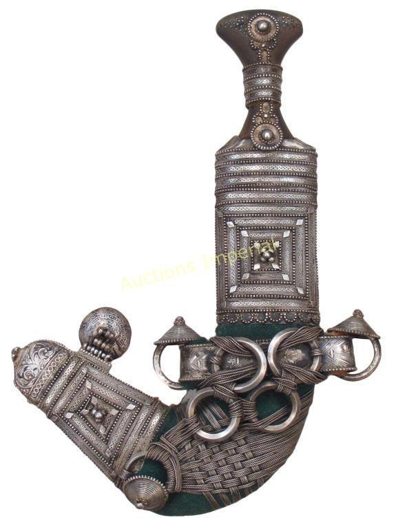 AN OMANI KHANJAR DAGGER: Of typical form, the horn grip with flared pommel and filigreed silver mounts. The curved, double-edged blade with central rib, wooden scabbard with heavy silver-embroidered fabric covering and large 