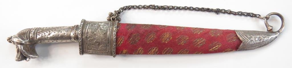 AN INDIAN KARD DAGGER: The grip wrought entirely of silver, terminating in a full-modelled tiger€™s head and engraved, the robust single-edged blade forged of patterned-welded damascus steel. In its silk-covered wooden 