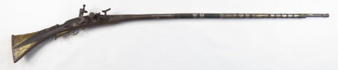 A MOROCCAN MUSKET: Of Taouzilt type, the hardwood stock of characteristic form, set with profiled brass and iron mounts. Mounted with a locally-produced snaphaunce lock featuring a sliding pan cover. The barrel with oct
