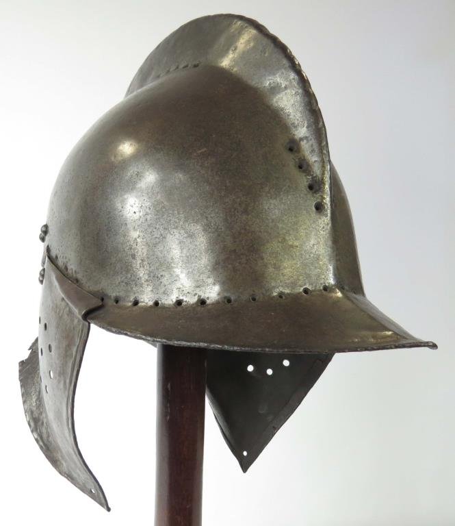 A BURGONET HELMET: German work, the skull wrought from a single piece of steel, with characteristic high comb, and peaked visor and neck guard. The earpieces embossed at the upper edge to suit the visor, the whole embel