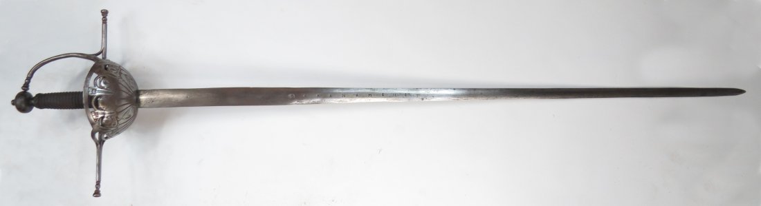 A SPANISH RAPIER SWORD: The steel cupguard chiseled with scallop shells surmounted by engraved flowers beneath the pierced, arched rim, the fabric guardapolvo intact. The guard of round section with long quillons and knuckle