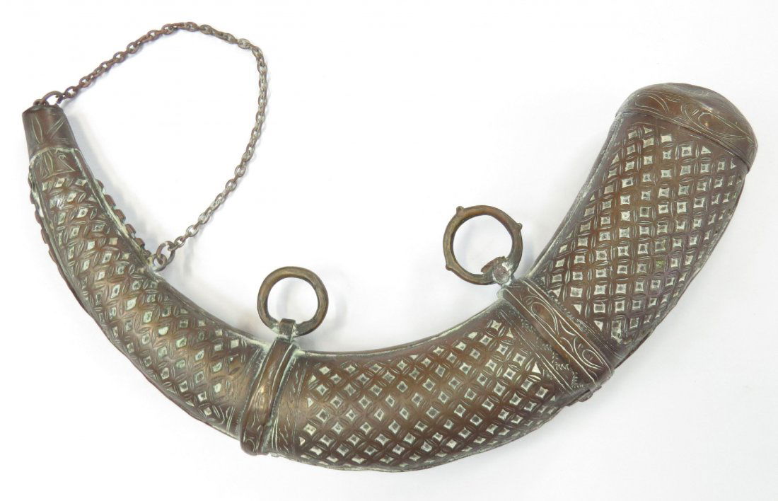 A MOROCCAN POWDERHORN: Covered entirely in brass and elaborately engraved overall in repeating geometrical motifs original captured cap intact.19th century. Worn. Overall length 34cm. Condition