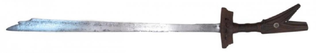 A MORO KAMPILAN SWORD: The finely-grained hardwood hilt of typical form, with bifurcate pommel and broad crossguard, carved overall, with iron guard and rattan grip-wrap intact. The long, single-edged blade expanding toward