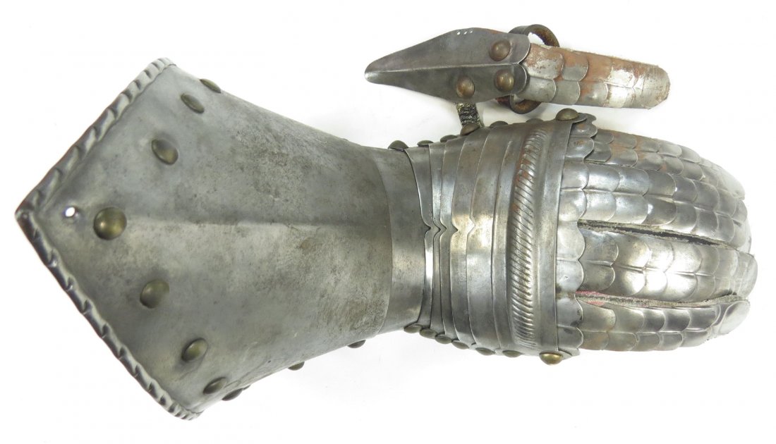 A VICTORIAN-ERA ARMOR GAUNTLET: Very well wrought, with individual fingers and thumb, and brass studs. Excellent detail throughout including embossed fingernails. Latter 19th century. Worn, areas of rust. Overall length 25.6cm