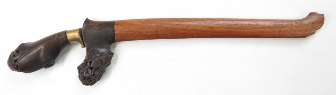 A SUMATRAN BADEK DAGGER: With finely-carved horn grip and scabbard locket, the recurved, single-edged and fullered blade of layered construction. In its wooden scabbard. Latter 19th century. Worn. Overall length 38.9cm. Condi