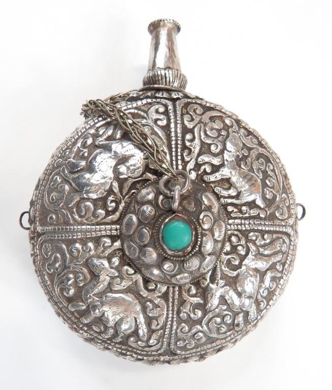 A FINE TIBETAN POWDER FLASK: Of circular form, finely wrought of embossed and engraved silver divided into in quadrants, each enclosing an animal surrounded by foliage. With lotus-form spout and central domed central plug decorat