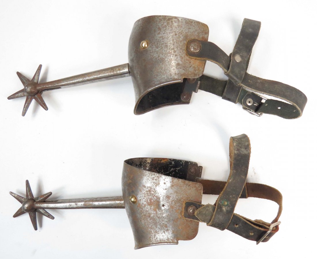 A PAIR OF VICTORIAN KNIGHTLY SPURS: With long, tapering, faceted shanks and six-pointed rowels. On their original steel armor heel plates with replaced leather straps. First half of the 19th century. Areas of rust. Overall length 32.5cm