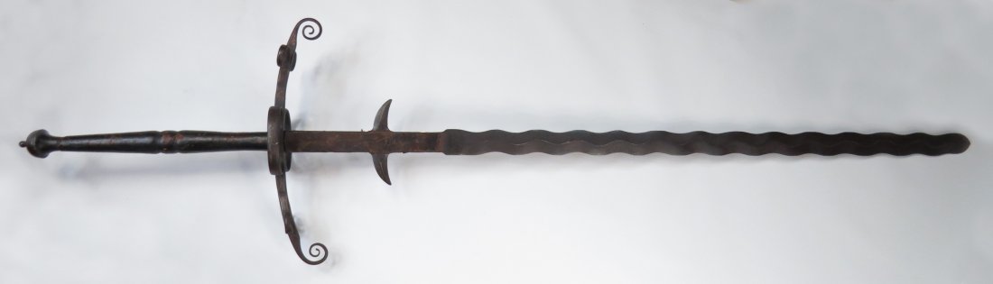 A RARE GERMAN TWO-HANDED SWORD: A characteristically massive weapon, the hilt elements exceptionally well-wrought, the pommel flared, the guard with double ring guards and complex quillons terminating in curled finials, the wooden g