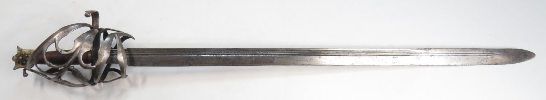 A RARE VENETIAN SCHIAVONA SWORD: The steel basket hilt wrought of characteristic complex profiled strips, curled quillon and integral thumbring. The fine “cat’s head” form pommel of bronze intricately engraved, with leather-cov