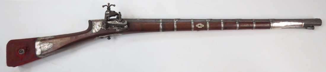AN OTTOMAN SHISHANA RIFLE: Rare in carbine length, made for a horseman. The dark walnut stock of characteristic form, embellished with embossed and engraved silver plaques. The butt covered in velvet and set with filigreed silv