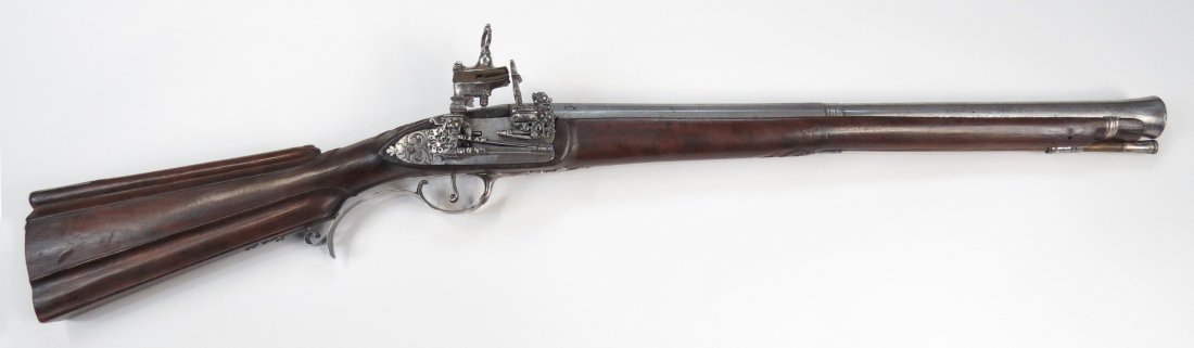 A RARE SPANISH BLUNDERBUSS: The dark hardwood stock with characteristic fluted butt carved with a floral spray at the breech. The mounts finely wrought of silver, comprising buttplate, triggerguard, counterplate, barrel band, ra