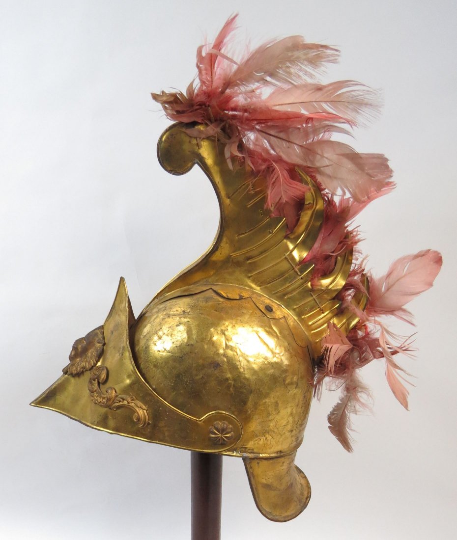 A VICTORIAN-ERA GRECO-ROMAN HELMET: Wrought of gilt brass with high, embossed crest retaining most original feathers, the broad, peaked visor with a lion’s head and baroque appliques, and curved neck guard. Original liner intact. Mid-